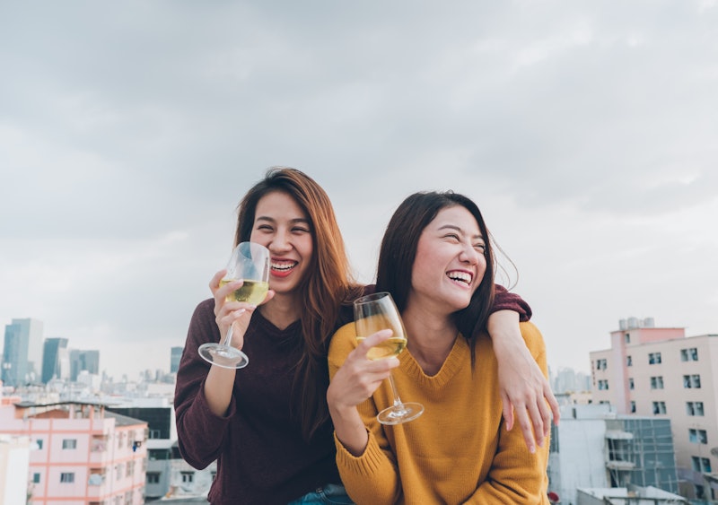 Two women are cuddled next to each other drinking wine and laughing on a rooftop. In numerology, lif...
