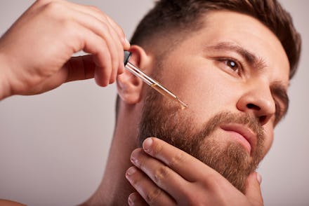 Close-up image of handsome man holding pipette with oil for beard