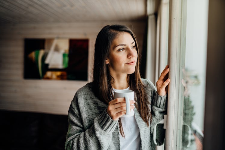 Young woman spending free time home.Self care,staying home.Enjoying view,gazing through to the windo...