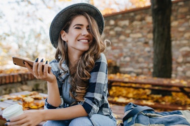 Pretty laughing girl with smartphone has a good time in autumn weekend. Outdoor portrait of lovable ...