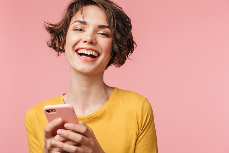 Image of a happy young beautiful woman posing isolated over pink wall background using mobile phone.