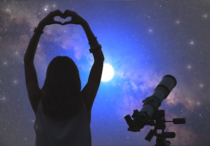 A woman makes a heart with her hands while stargazing at night. 