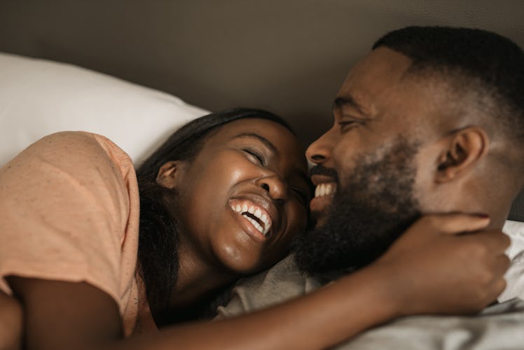 Affectionate young African American couple laughing and hugging each other while lying in bed togeth...