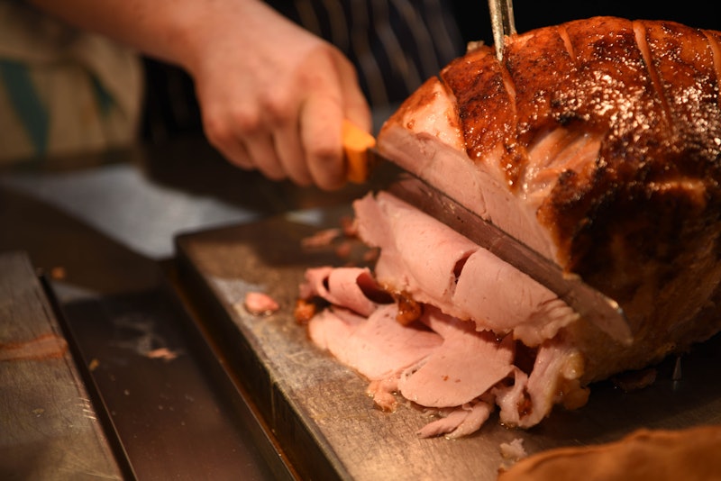 food photography image of roast gammon ham joint of meat being carved with mans hand holding a knife...