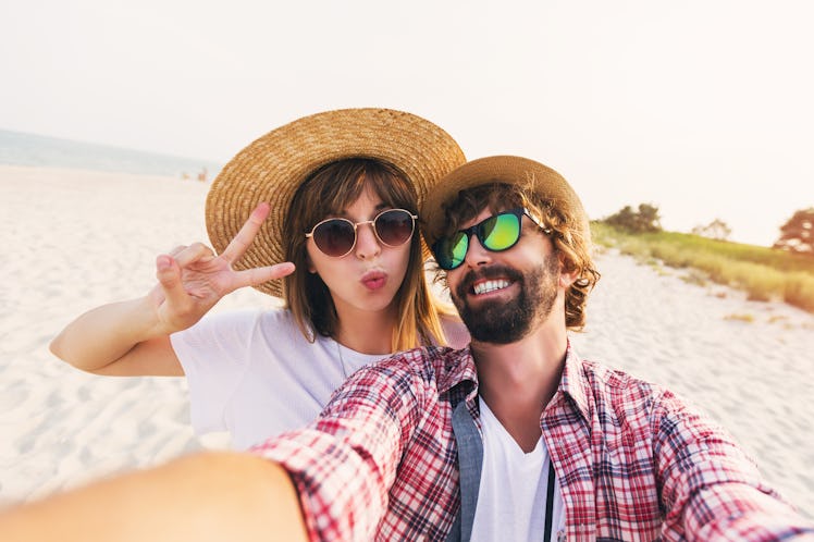 Happy young  couple in love making a selfie on phone at the beach on a sunny summer day. Pretty girl...