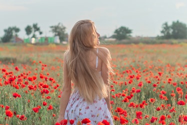 A woman with long blonde hair wearing a white sundress with flowers on it twirls in a flower field w...