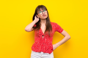 Young woman over yellow wall having doubts