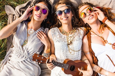 Three cute hippie girl lying on the plaid outdoors, best friends having fun and laughing, play ukule...