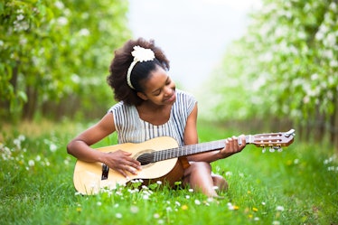 Outdoor portrait of a young beautiful african american woman playing guitar - Black people