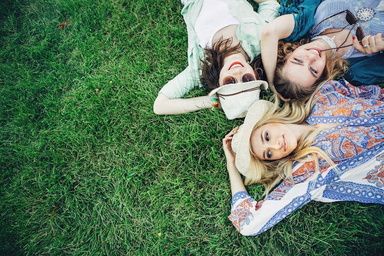 Trendy Hipster Girls Relaxing on the Grass . Summer lifestyle portrait of three hipster women laying...