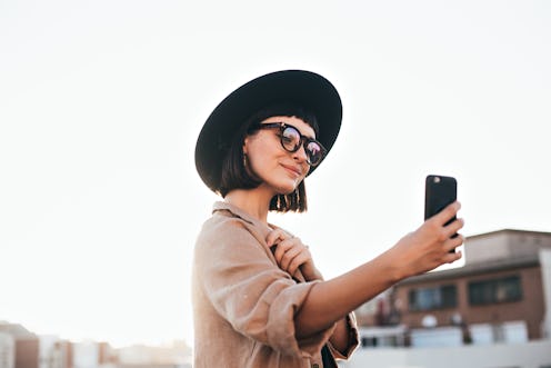 Cute and pretty fashion trendy and hipster millennial woman or girl makes selfie on smartphone camer...