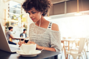 Portrait of an attractive young woman with earphones using laptop at a cafe. African american woman ...