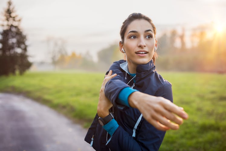 Woman stretching at park while listening to music. Young woman working out at sunset. Healthy sport ...