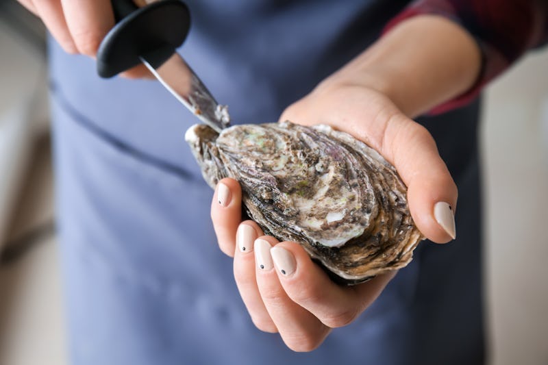 Woman opening raw oyster with knife, closeup