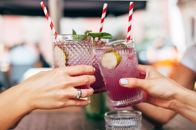 A group of friends holding lavender cocktails toast before drinking.