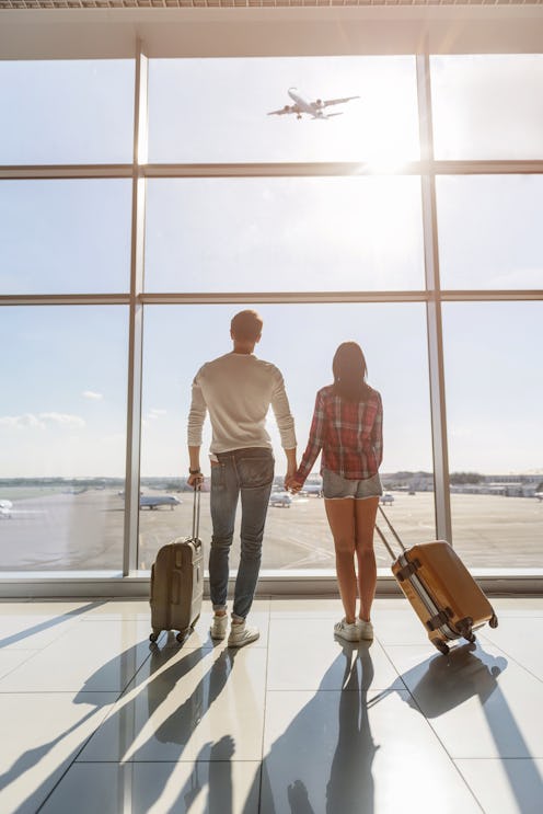 Dreamful loving couple is ready for travel. They are standing near window at airport and looking at ...