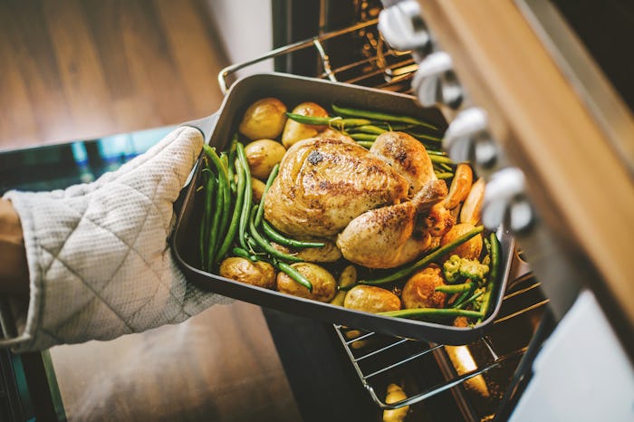 Cook taking ready fried baked chicken with vegetables from the oven. Home cooking concept.