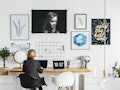 A blonde woman with a black and white flannel sits at a trendy desk in her home.