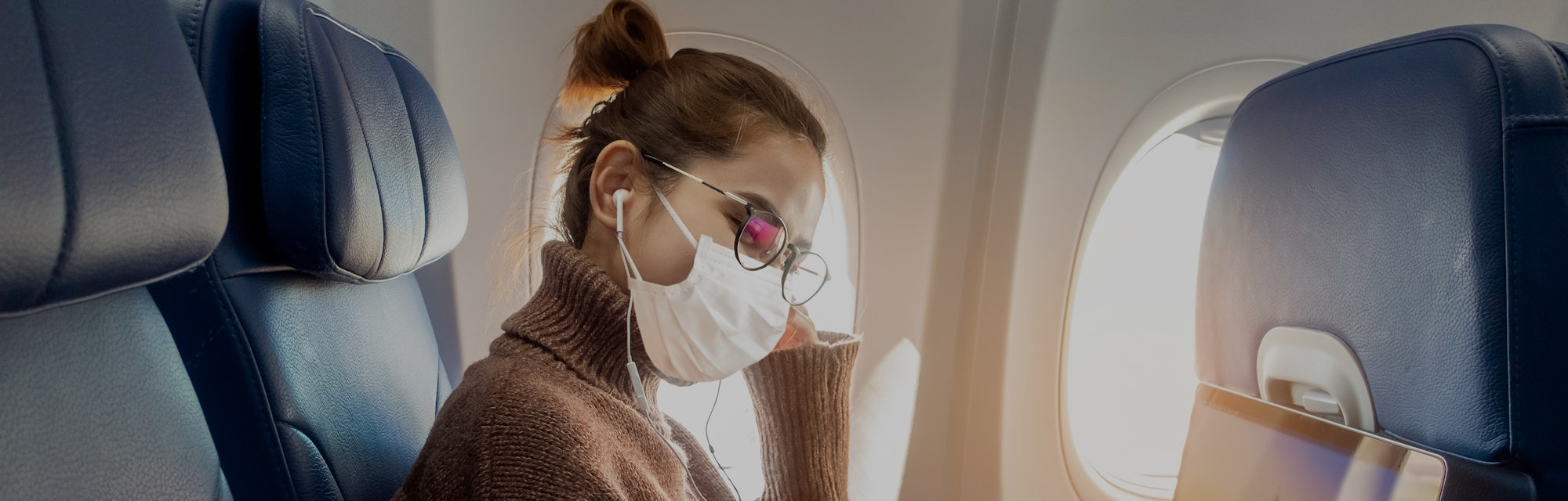 A young woman wearing face mask is traveling on airplane , New normal travel after covid-19 pandemic...