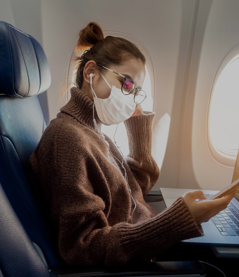 A young woman wearing face mask is traveling on airplane , New normal travel after covid-19 pandemic...