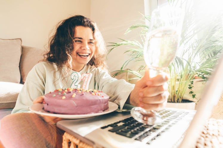 Woman blowing out the candle on the birthday cake and making video call. Girl celebrating birthday o...