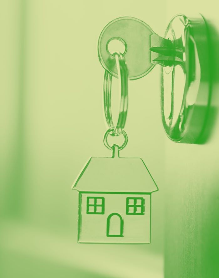 House key on a house shaped silver keyring in the lock of a entrance  brown door