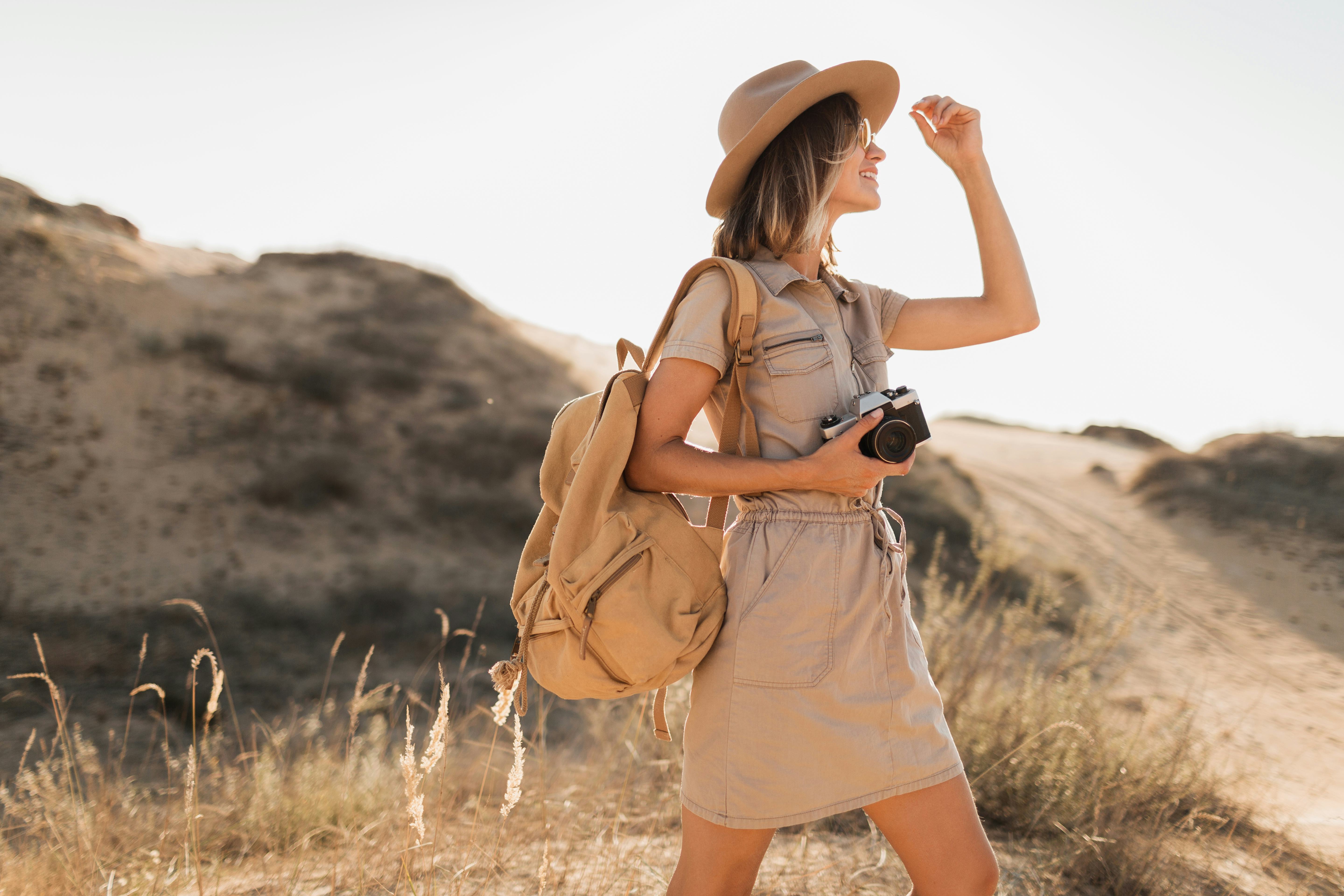 stylish young woman in khaki dress walking in desert, traveling in Africa on safari, wearing hat and...