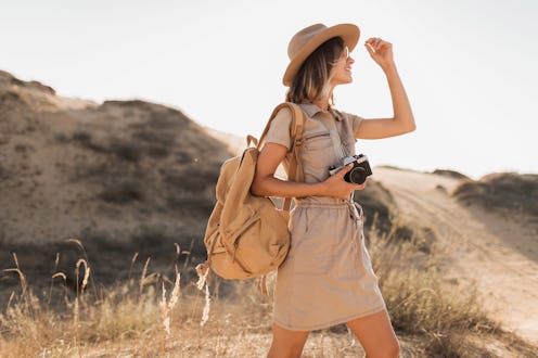 stylish young woman in khaki dress walking in desert, traveling in Africa on safari, wearing hat and...