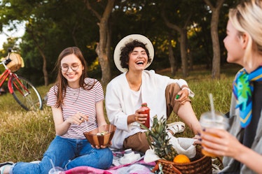 Smiling girls sitting on picnic blanket joyfully laughing spending time together on picnic in park