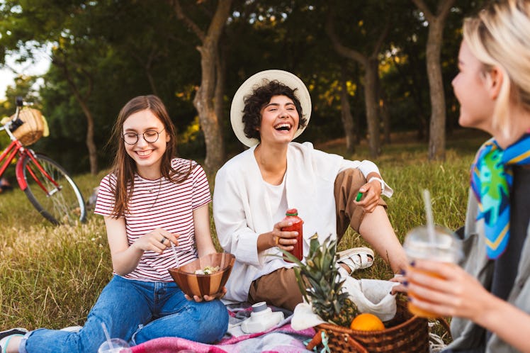 Smiling girls sitting on picnic blanket joyfully laughing spending time together on picnic in park