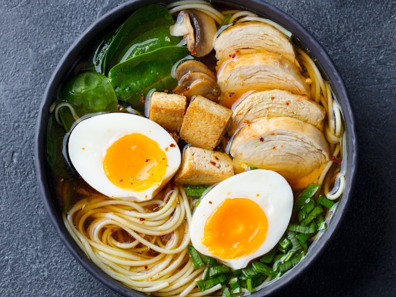 A black bowl of ramen with chicken, tofu, vegetables and egg.