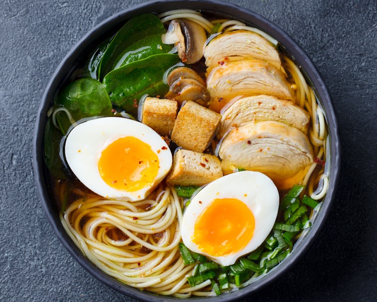 A black bowl of ramen with chicken, tofu, vegetables and egg.