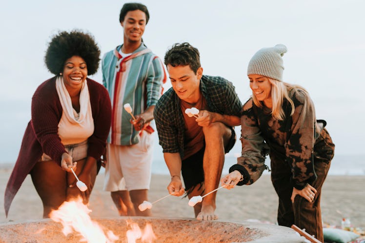 A group of happy friends roast s'mores over a fire pit on the beach, for which they need fire captio...