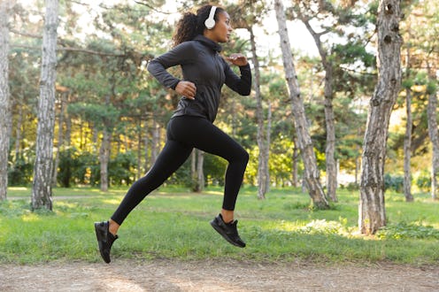 Image of feminine woman 20s wearing black tracksuit and headphones working out while running through...