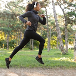 Image of feminine woman 20s wearing black tracksuit and headphones working out while running through...