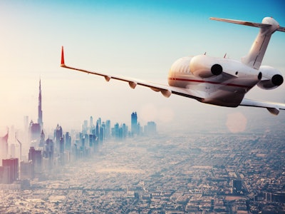 Private jet plane flying above Dubai city in beautiful sunset light. Modern and fastest mode of tran...
