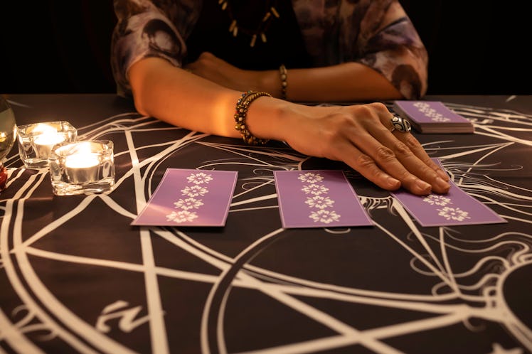Tarot reader picking tarot cards.Tarot cards face down on table near burning candles and crystal bal...