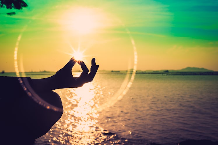 Silhouette, a hand of woman meditating in a Yoga pose or Lotus position at the Sea in Sunset and ref...
