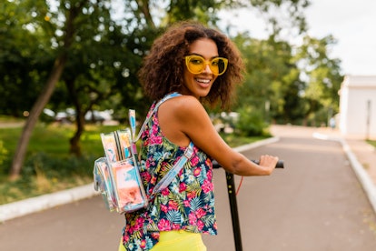 A stylish woman dressed in yellow sunglasses, a floral top, and yellow pants smiles while riding an ...