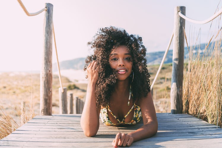 Beautiful young black woman lies down on a wooden bridge at the beach.
