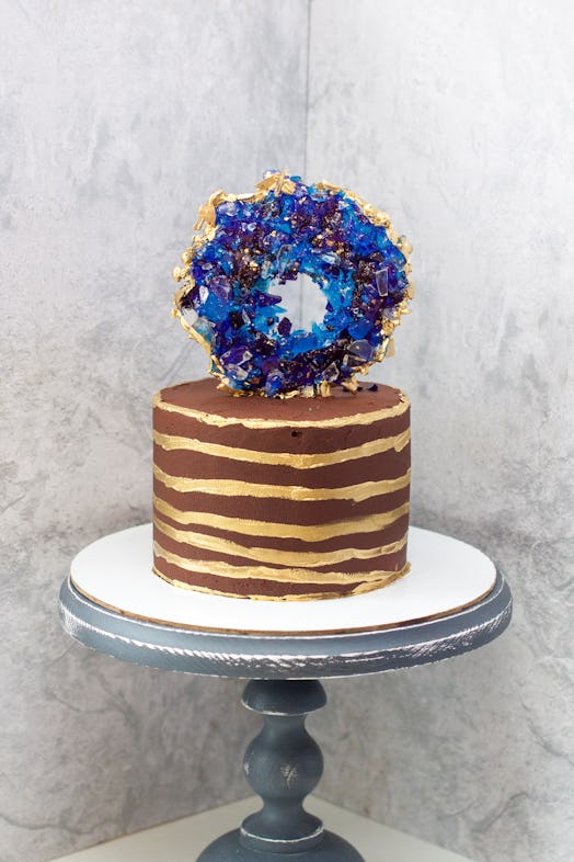 Chocolate modern cake with golden stripes and blue isomalt geode. Grey background.