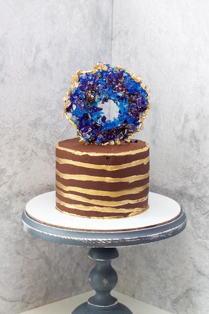 Chocolate modern cake with golden stripes and blue isomalt geode. Grey background.