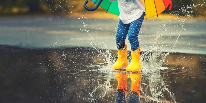 Feet of child in yellow rubber boots jumping over a puddle in the rain
