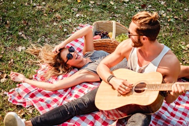 Man playing guitar to his girl on a picnic