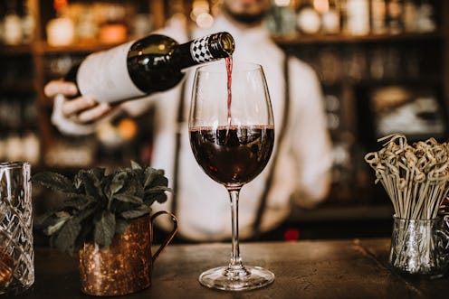 Bartender pouring red wine from a bottle in a wine glass, selective point of view on a wine glass