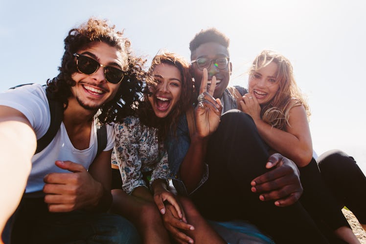 Excited young friends taking selfie outdoors. Diverse group of men and women sitting together and ta...