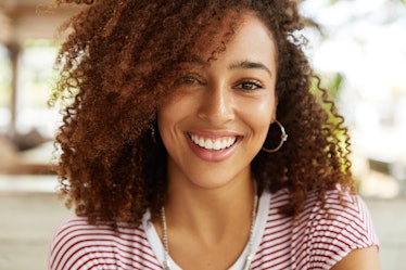 Close up shot of adorable African American woman has broad smile, wears striped t shirt, being in go...