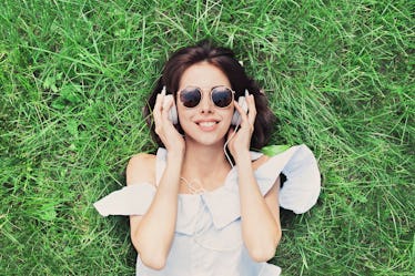 Beautiful happy young woman with headphones listening music lying on grass. Summer girl portrait