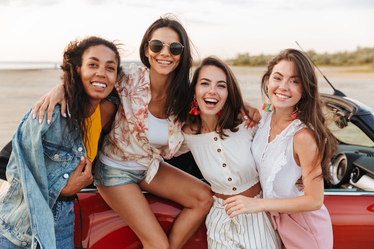 Picture of amazing young happy smiling cheery women friends posing near car outdoors at the beach.