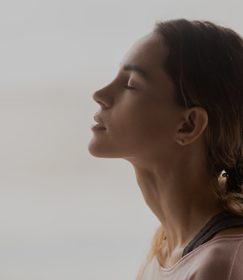 Serene young woman taking deep breath of fresh air relaxing meditating with eyes closed enjoying pea...